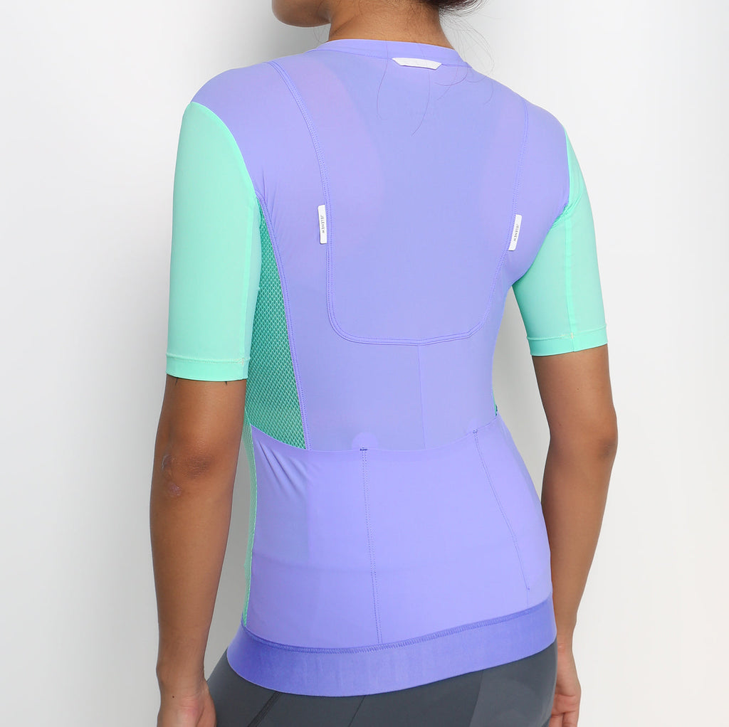 Back view of woman wearing purple and mint green Hourglass Short Sleeve Training Jersey with CurveTec technology for women cyclists