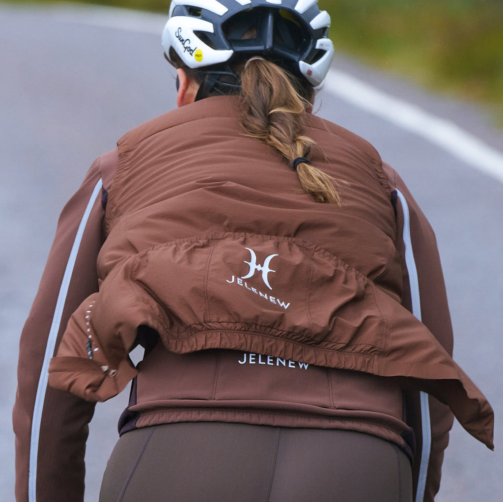 Cyclist wearing a brown lightweight package cycling gilet on a road, showing insulation and compact design for comfort and warmth