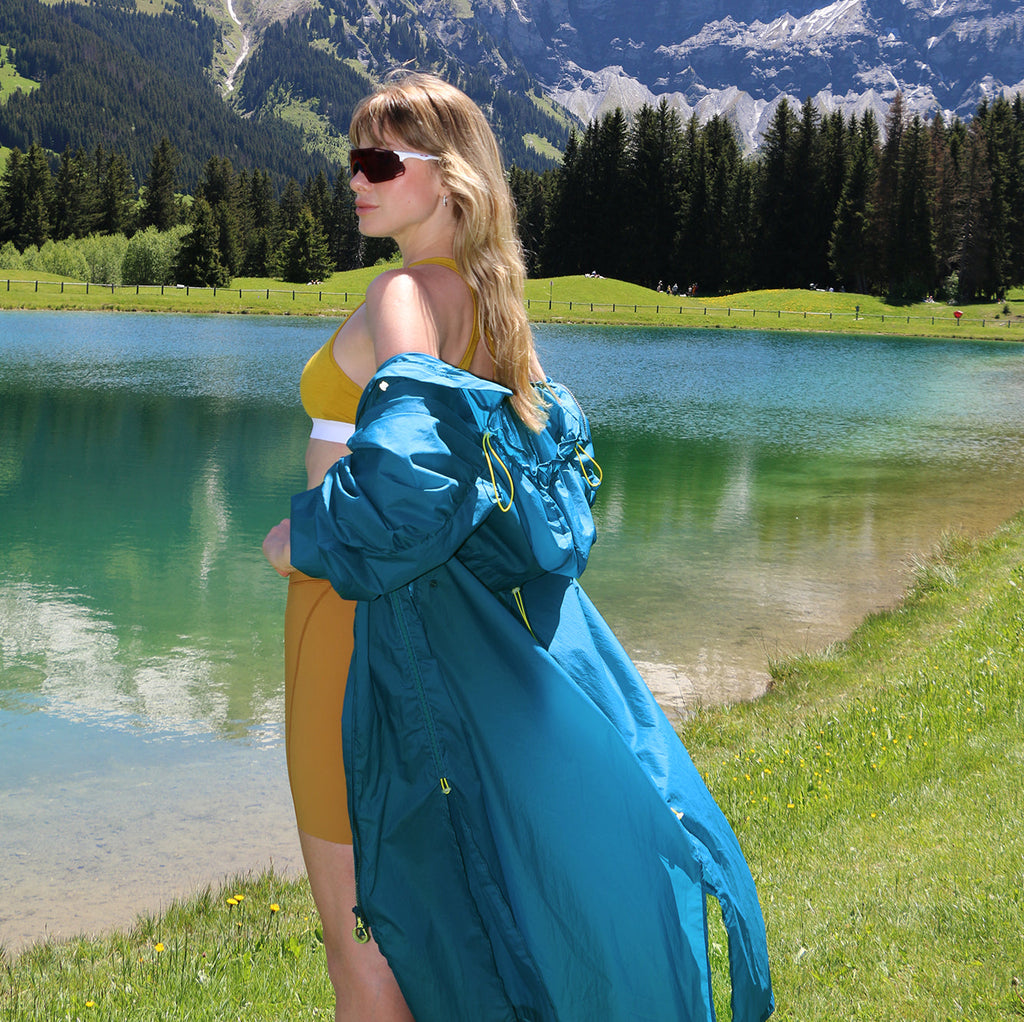 Woman wearing Mont Blanc ultralight long windproof jacket by a lake with mountains in background