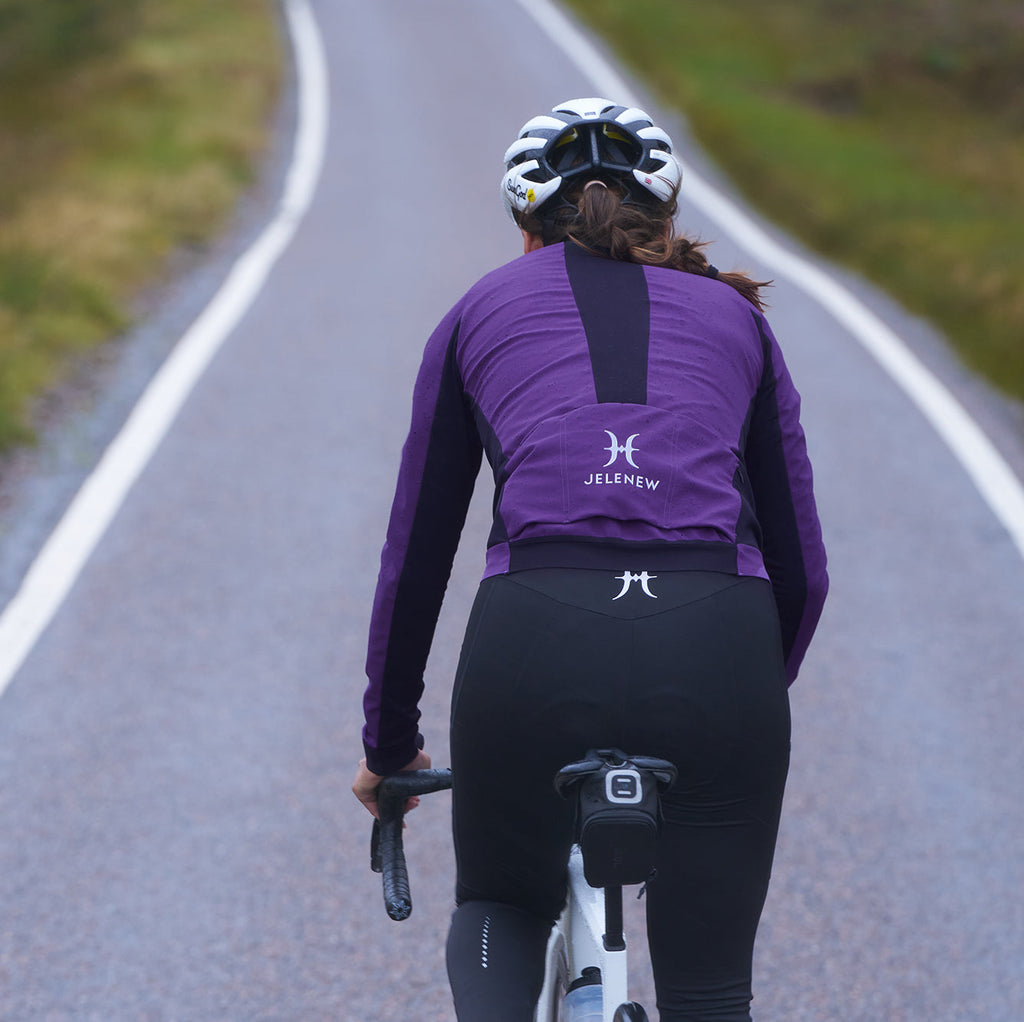 Cyclist wearing purple 3L Core Rain Jacket riding on road in autumn setting