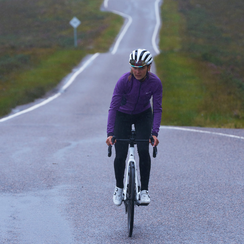 Cyclist wearing purple 3L Core Rain Jacket riding on wet road in autumn weather
