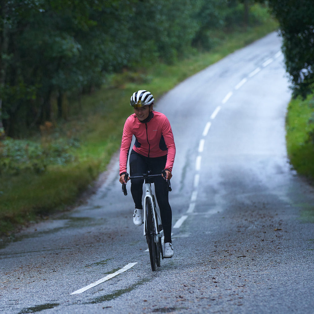 cyclist wearing pink 3L Core Rain Jacket riding on wet road through forested area